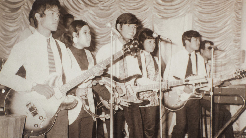 A black and white image of six male and female musicians performing on stage.